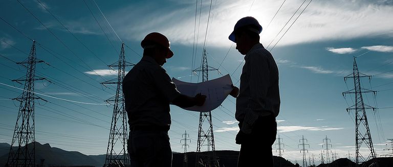 Silhouette von zwei Ingenieuren mit Bauhelmen, die im Elektrizitätswerk stehen und über einen Plan diskutieren