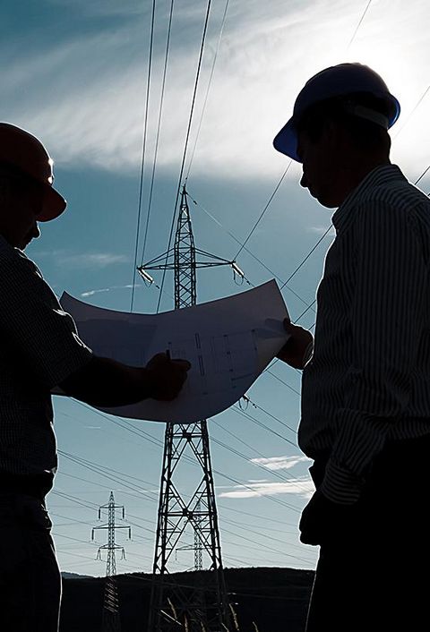 Silhouette von zwei Ingenieuren mit Bauhelmen, die im Elektrizitätswerk stehen und über einen Plan diskutieren
