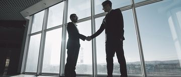 Geschäftspartner stehen in einem Gewerberaum vor einer großen Glasfront und schütteln sich die Hände. Geschäftspartner stehen in einem Gewerberaum vor einer großen Glasfront und schütteln sich die Hände.