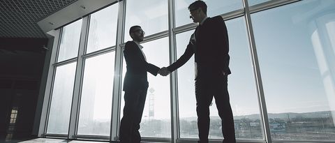 Geschäftspartner stehen in einem Gewerberaum vor einer großen Glasfront und schütteln sich die Hände. Geschäftspartner stehen in einem Gewerberaum vor einer großen Glasfront und schütteln sich die Hände.
