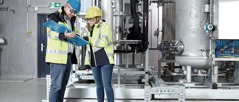 Power-to-Gas in Wyhlen Zwei Energiedienst-Mitarbeiter mit Schutzhelm und Warnjacken stehen in der Power-to-Gas in Wyhlen vor den Maschinen und beraten sich.
