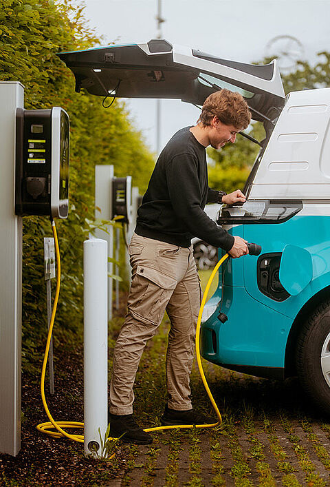 Elektro-Transporter wird an einer Ladesäule auf einem Parkplatz geladen.