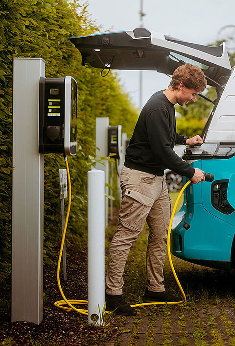 Elektro-Transporter wird an einer Ladesäule auf einem Parkplatz geladen.