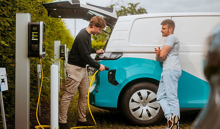 Elektro-Transporter wird an einer Ladesäule auf einem Parkplatz geladen.