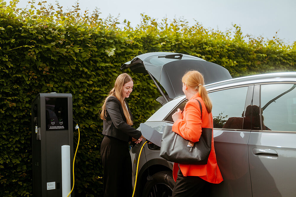 Zwei Personen stehen neben einem Elektroauto, das an einer Ladesäule angeschlossen wird.
