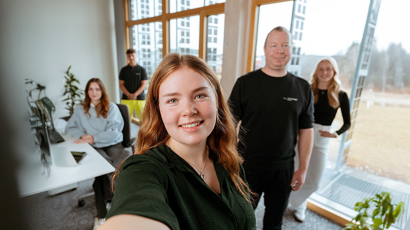 Mehrere Personen in einem hellen Büro mit Schreibtisch, Fenstern und Pflanzen.