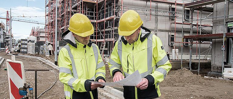 Zwei Ingenieure von NaturEnergie betrachten einen Bauplan auf einer Baustelle für eine energieeffiziente Wohnanlage mit zukunftsweisenden Energielösungen in Rheinfelden