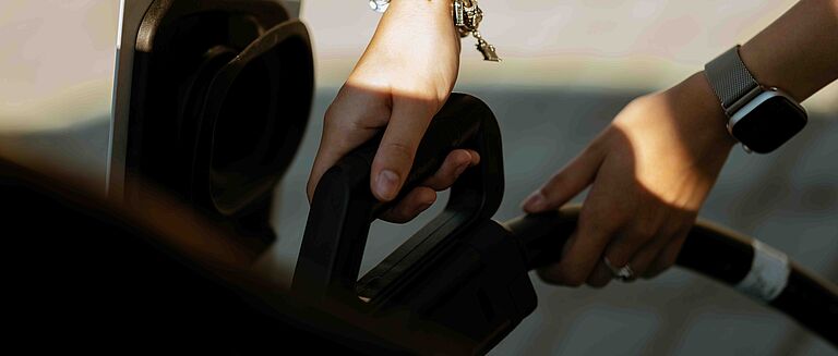 Hände stecken Ladekabel in Elektroauto