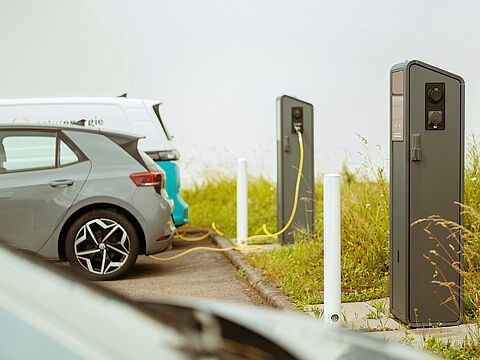 Elektroautos laden an zwei Ladesäulen auf einem Parkplatz im Freien.