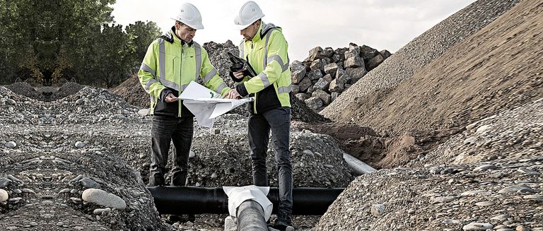 Wärme- und Energielösungen. Ingenieure von NaturEnergie besprechen einen Plan zur Erstellung eines Nahwärmenetzes auf einer Baustelle