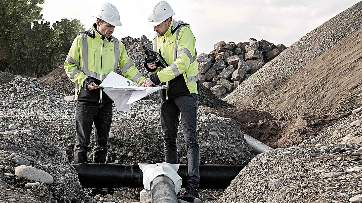 Wärme- und Energielösungen. Ingenieure von NaturEnergie besprechen einen Plan zur Erstellung eines Nahwärmenetzes auf einer Baustelle