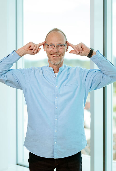 Person steht im Büro und zeigt mit den Fingern auf den Kopf.