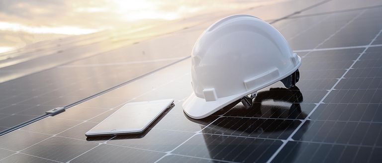 Weißer Bauhelm und ein Tablet auf dem Solarpaneel in einem Photovoltaik-Kraftwerk bei Sonnenaufgang