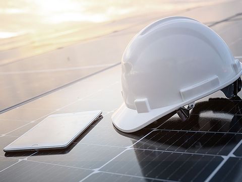 solar Wartung Instandhaltung Weißer Bauhelm und ein Tablet auf dem Solarpaneel in einem Photovoltaik-Kraftwerk bei Sonnenaufgang
