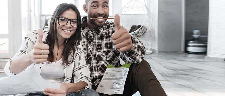 Foto von glücklichen Kunden daheim, die mit Dokumenten auf dem Boden arbeiten. Schauen Sie sich die Kamera an, während Sie die Daumen nach oben ziehen.