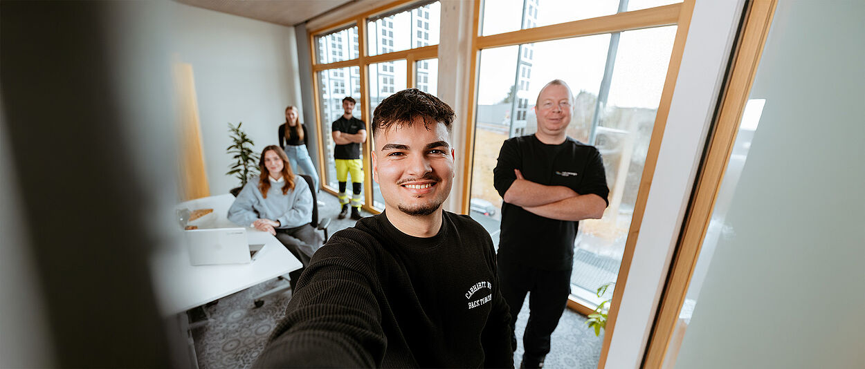 Mehrere Personen in einem modernen Büro mit Schreibtisch, Fenstern und Pflanzen