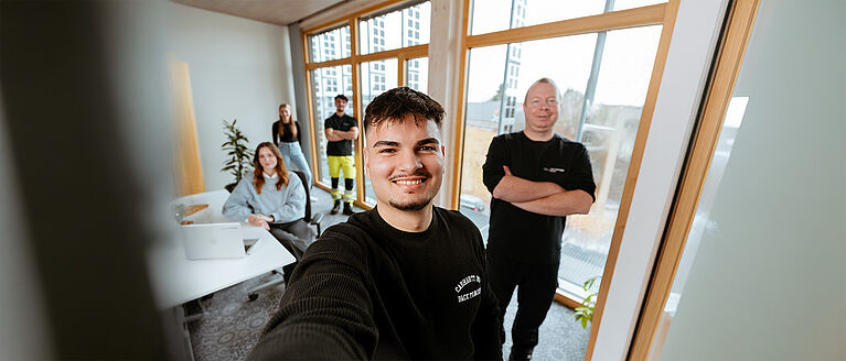 Mehrere Personen in einem modernen Büro mit Schreibtisch, Fenstern und Pflanzen