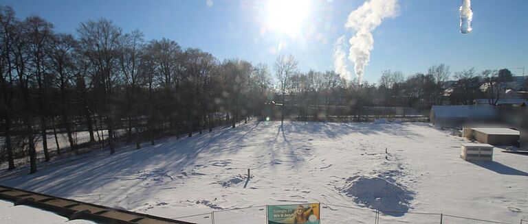 Schneebedecktes Baugrundstück für Seniorenwohnheim mit Sonne und Rauchwolke.