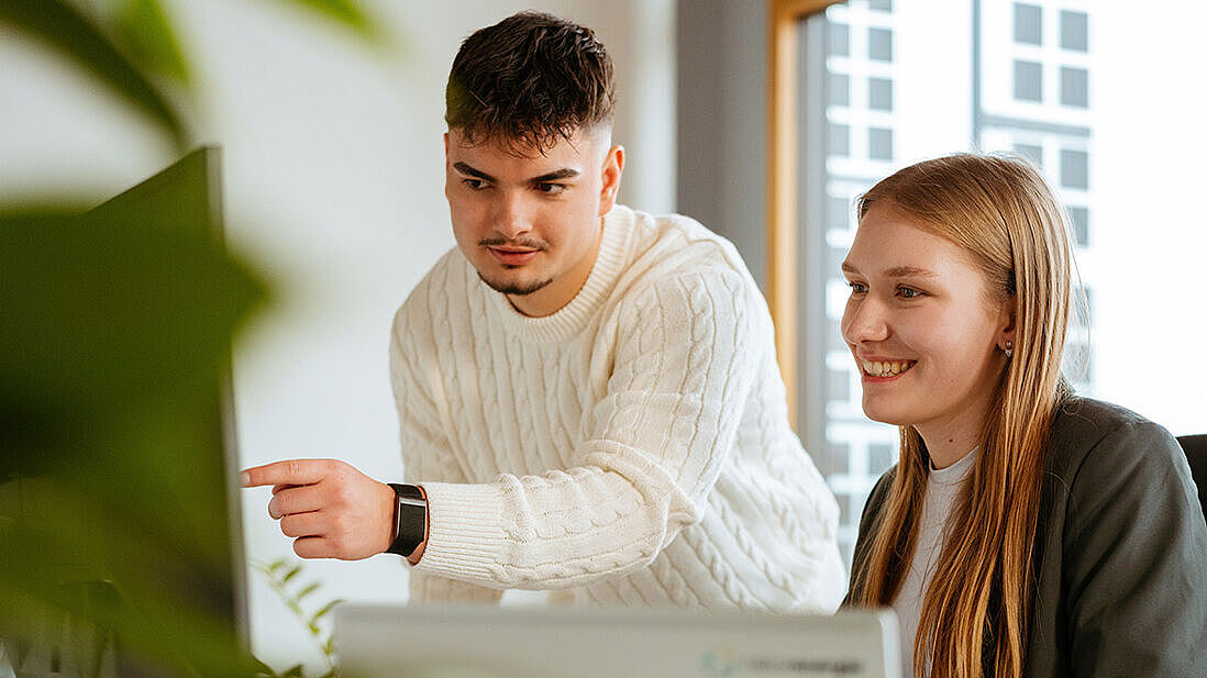 Zwei Personen arbeiten gemeinsam an einem Schreibtisch mit einem Laptop in einem Büro.