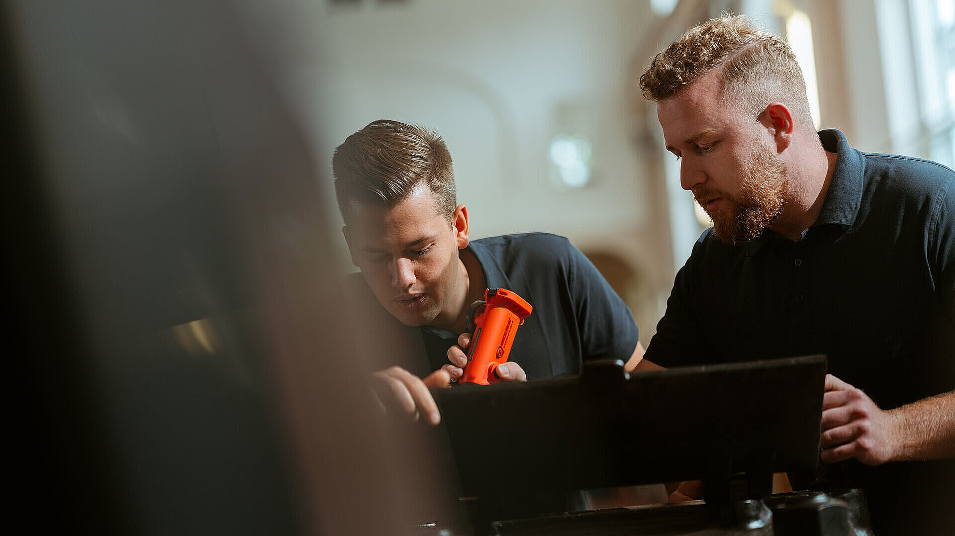 Zwei Mitarbeiter untersuchen ein technisches Gerät und schauen konzentriert auf eine Anlage.