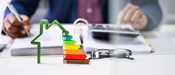Geschäftsmann Hausmodells mit Energieeffizienz Geschäftsmann, der mit dem Rechner in der Nähe des Hausmodells mit Energieeffizienz-Rate arbeitet
