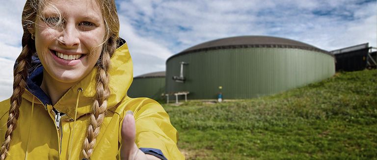 Frau mit gelber Regenjacke vor einer Biogasanlage, sie zeigt den Daumen hoch