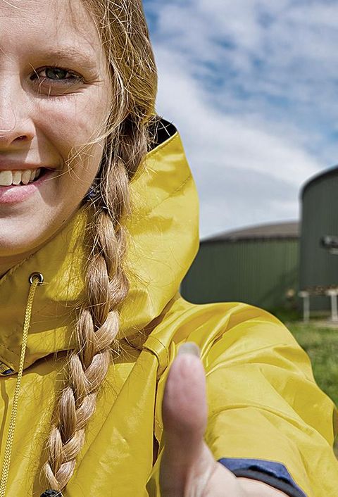 Frau mit gelber Regenjacke vor einer Biogasanlage, sie zeigt den Daumen hoch