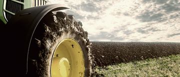 Landwirtschaft Traktorrad Teilansicht eines Traktors, der auf einem Feld bei schönem Wetter und bewölktem Himmel steht