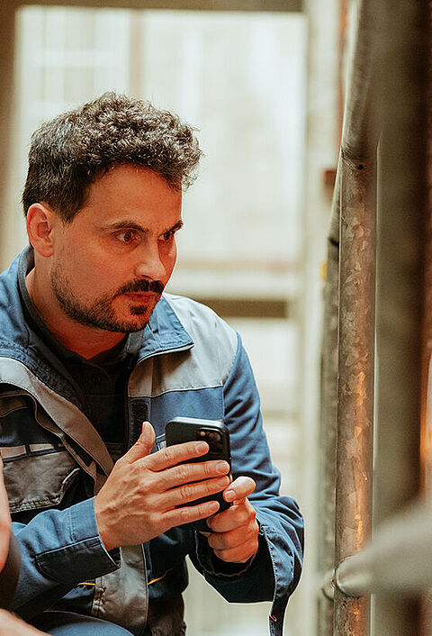Zwei Personen prüfen mithilfe eines Smartphones eine technische Anlage in einem Heizungsraum.
