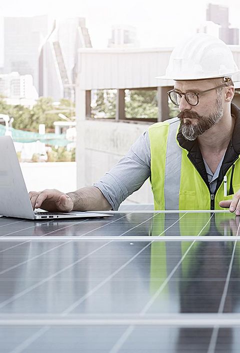 Ingenieur von Solarkraftwerken auf dem Dach, untersucht Photovoltaik-Paneele. Konzept der alternativen Energie und ihrer Dienstleistung. Gerätetechniker verwendet Laptop für die Wartung von Elektrotechnik