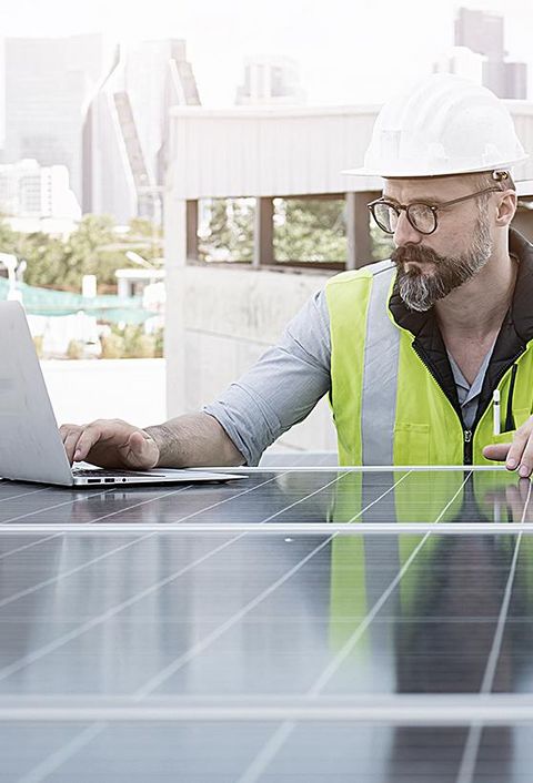 Ingenieur von Solarkraftwerken auf dem Dach, untersucht Photovoltaik-Paneele. Konzept der alternativen Energie und ihrer Dienstleistung. Gerätetechniker verwendet Laptop für die Wartung von Elektrotechnik