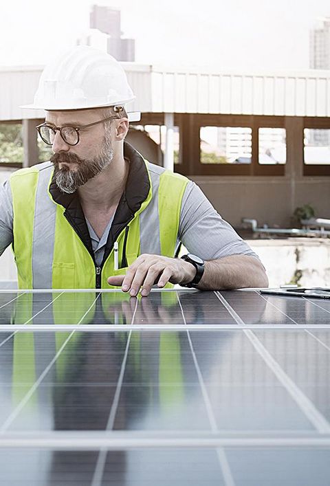 Ingenieur von Solarkraftwerken auf dem Dach, untersucht Photovoltaik-Paneele. Konzept der alternativen Energie und ihrer Dienstleistung. Gerätetechniker verwendet Laptop für die Wartung von Elektrotechnik