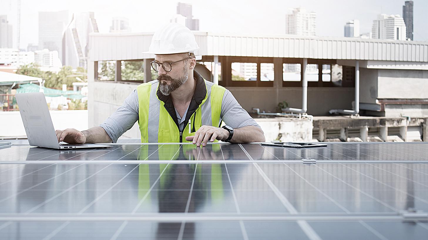 Ingenieur von Solarkraftwerken auf dem Dach, untersucht Photovoltaik-Paneele. Konzept der alternativen Energie und ihrer Dienstleistung. Gerätetechniker verwendet Laptop für die Wartung von Elektrotechnik