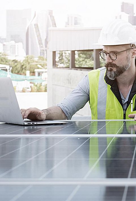 Ingenieur von Solarkraftwerken auf dem Dach, untersucht Photovoltaik-Paneele. Konzept der alternativen Energie und ihrer Dienstleistung. Gerätetechniker verwendet Laptop für die Wartung von Elektrotechnik